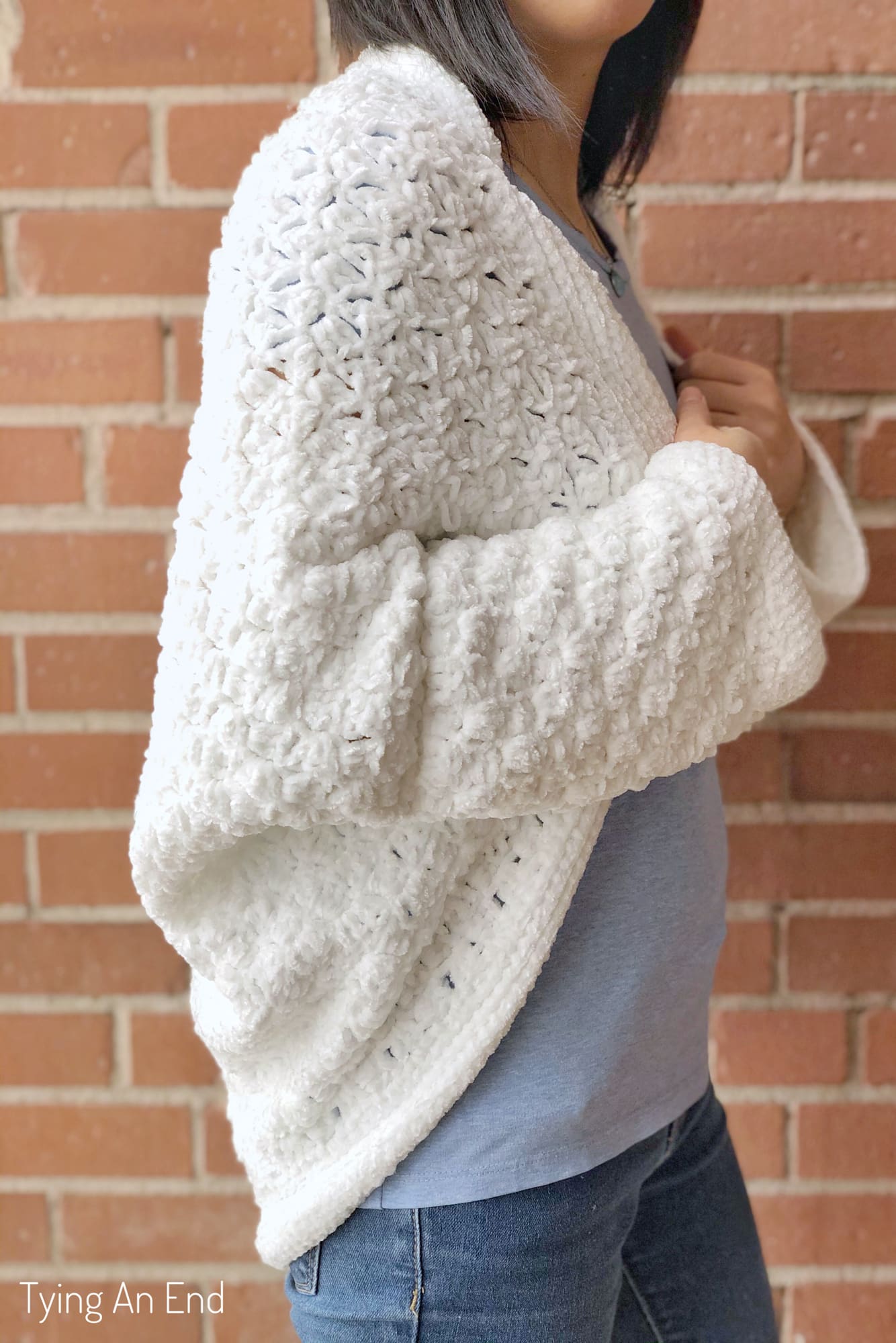 woman wearing white crochet c2c cocoon shrug in front of a brick wall