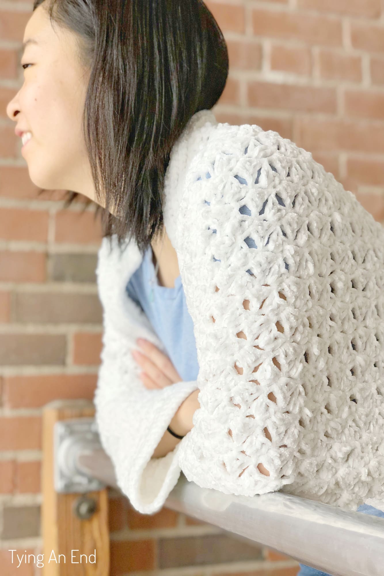 woman wearing white crochet c2c cocoon shrug in front of a brick wall