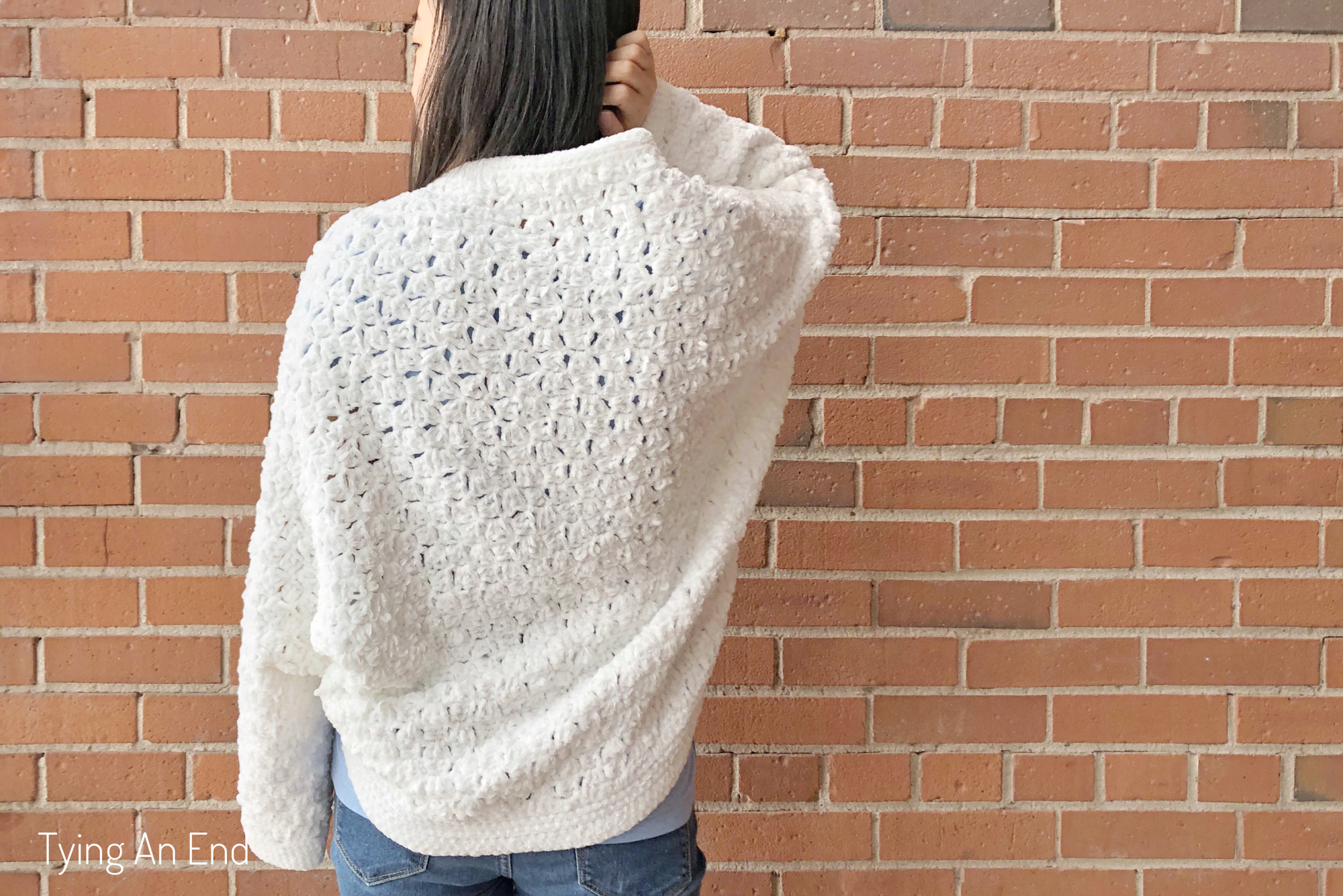 woman wearing white crochet c2c cocoon shrug in front of a brick wall