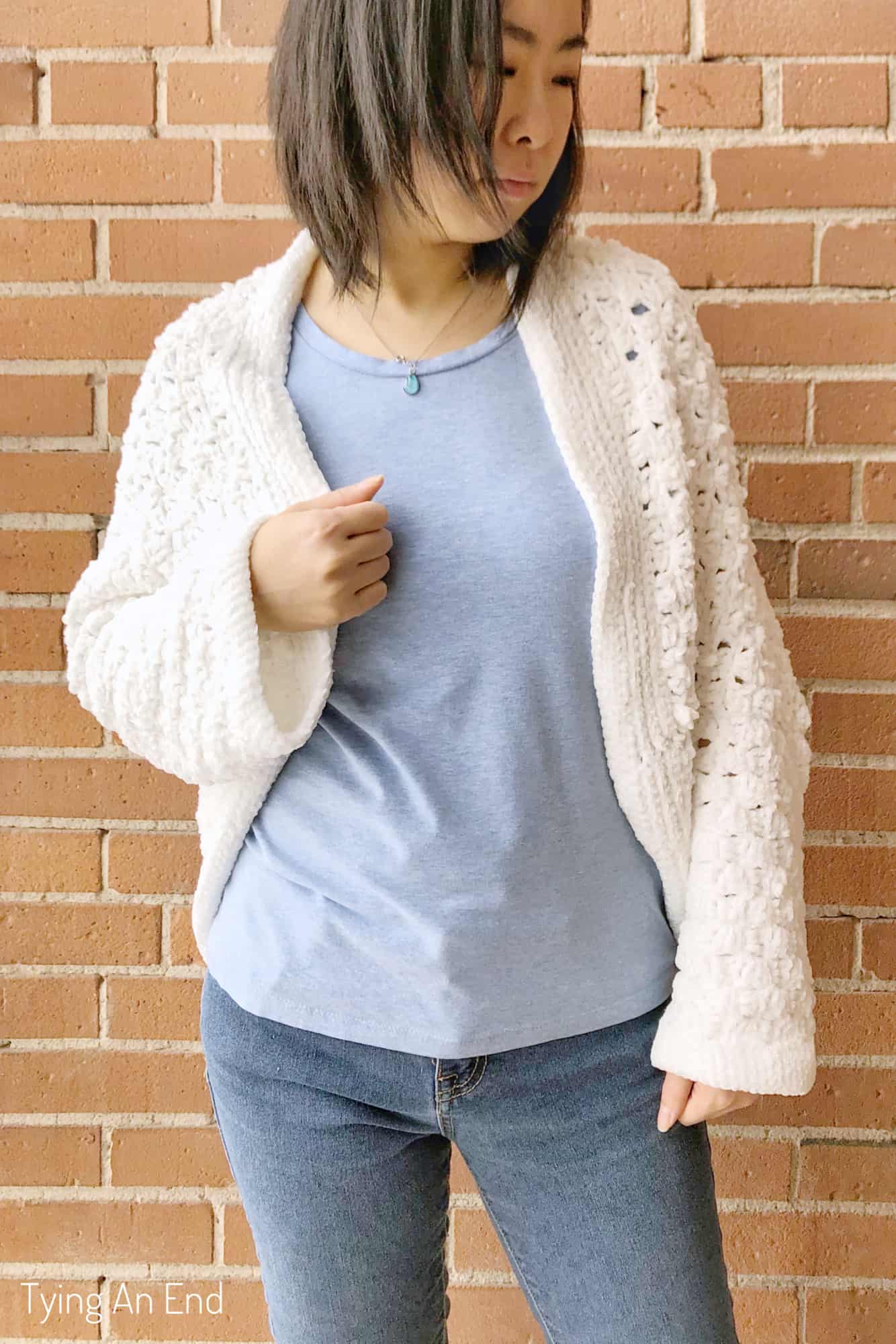 woman wearing white crochet c2c cocoon shrug in front of a brick wall