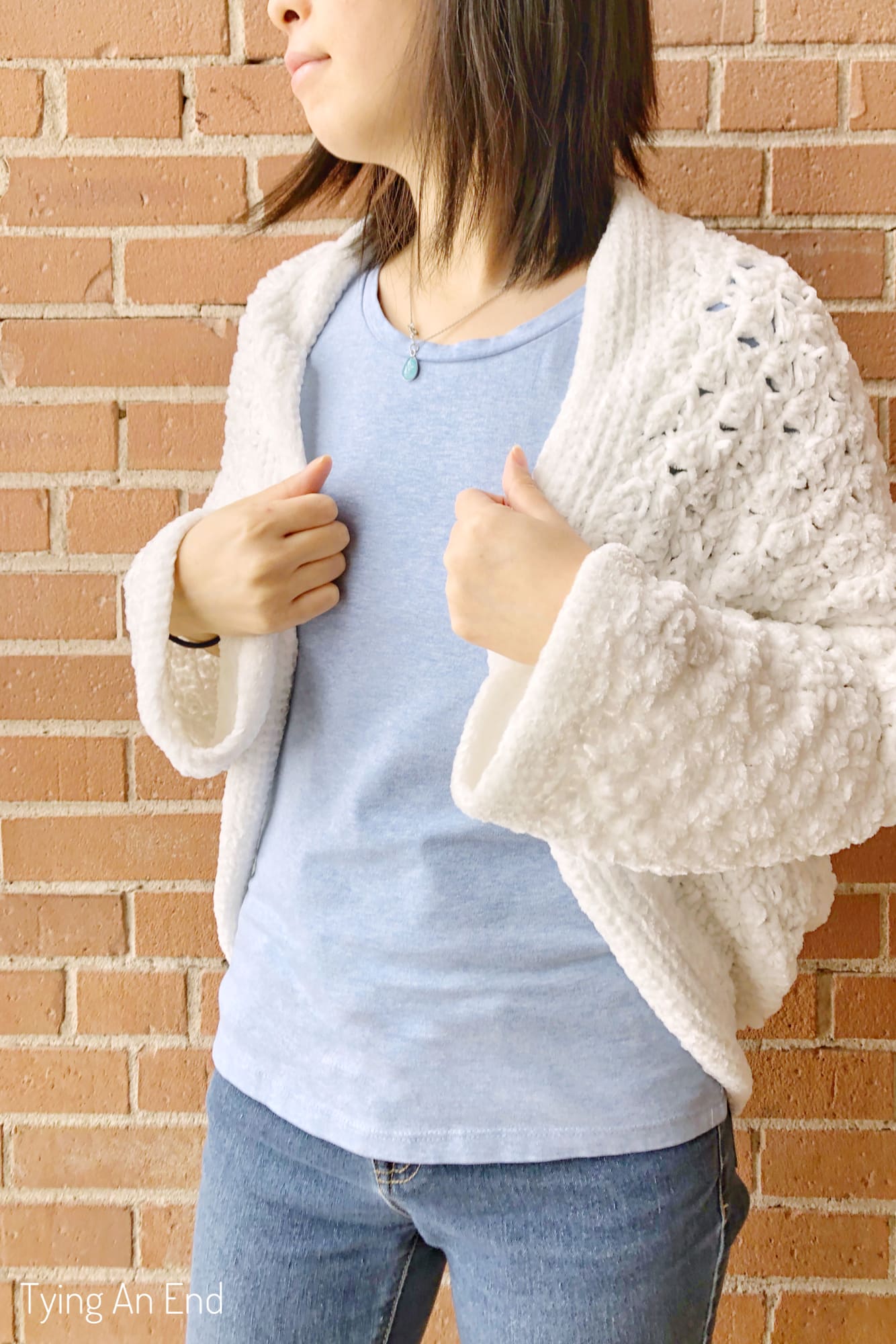 woman wearing white crochet c2c cocoon shrug in front of a brick wall