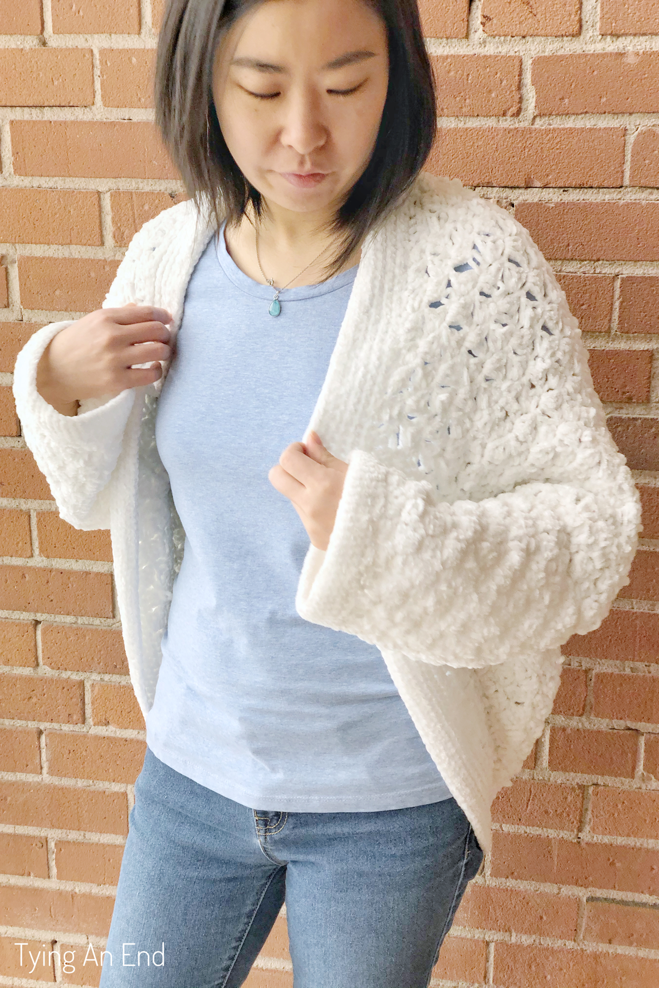 woman wearing white crochet c2c cocoon shrug in front of a brick wall