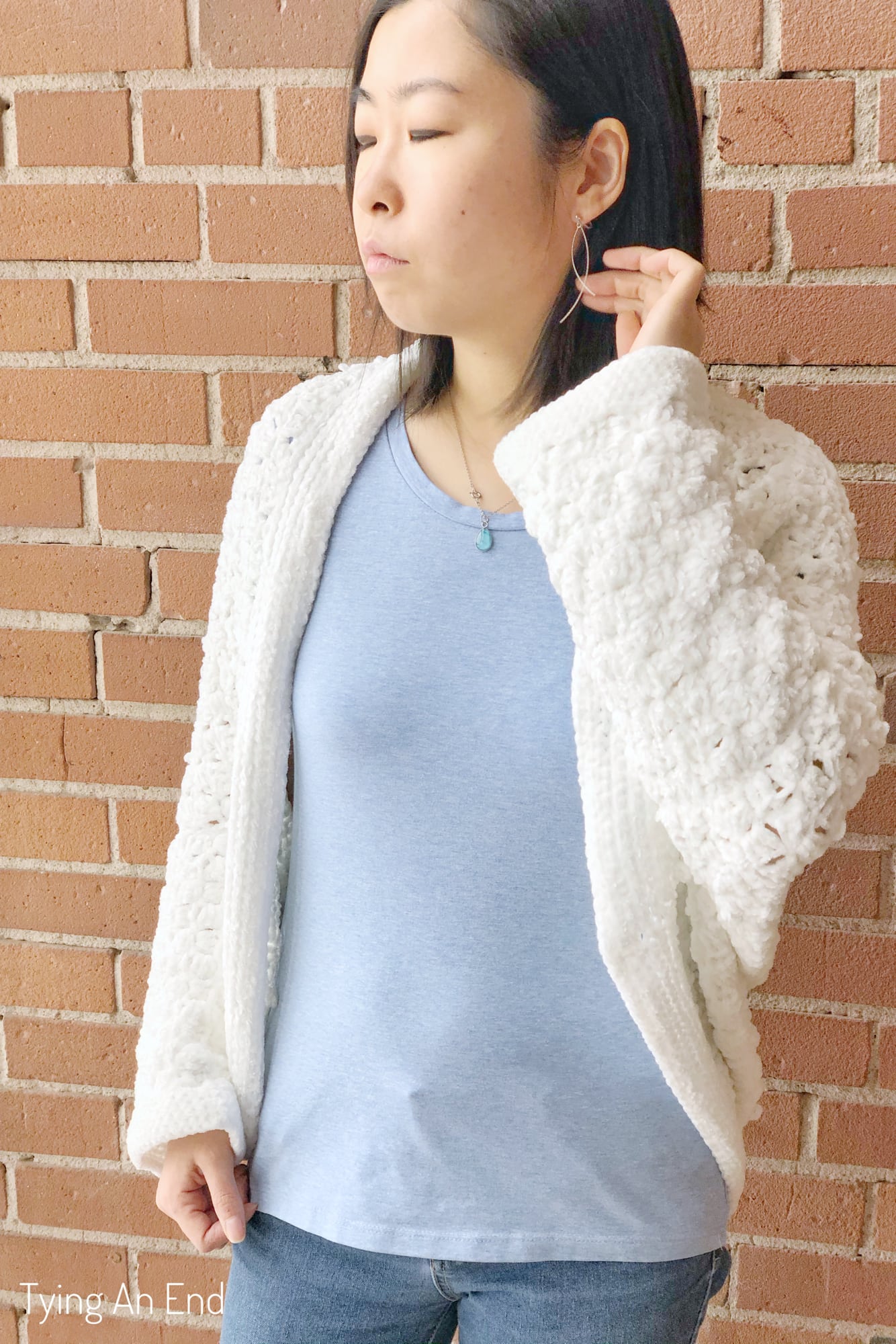 woman wearing white crochet c2c cocoon shrug in front of a brick wall