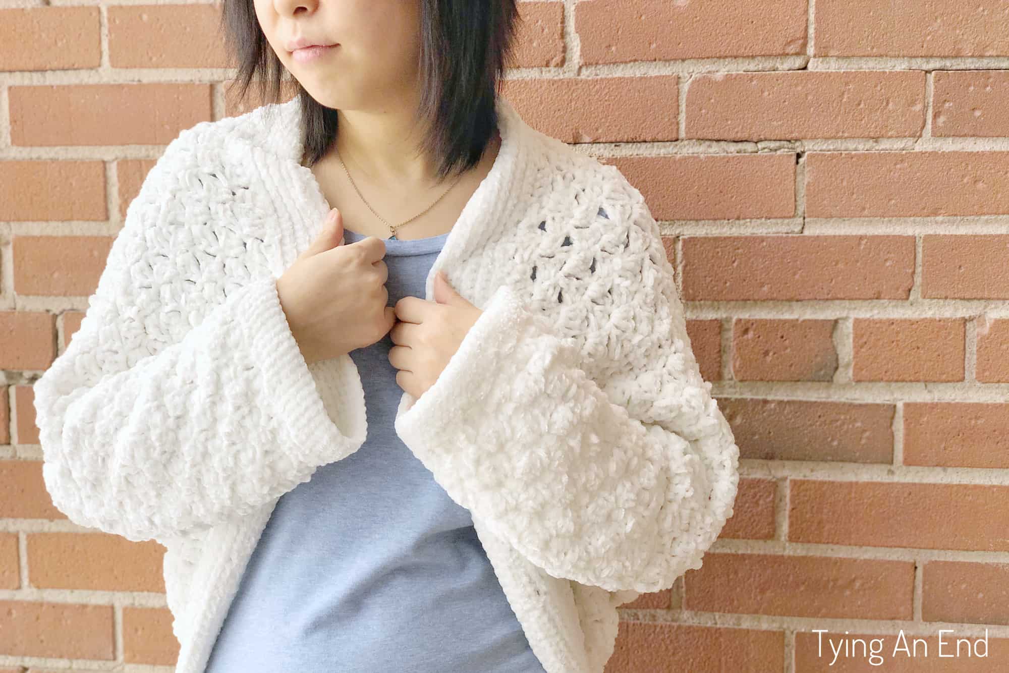 woman wearing white crochet c2c cocoon shrug in front of a brick wall