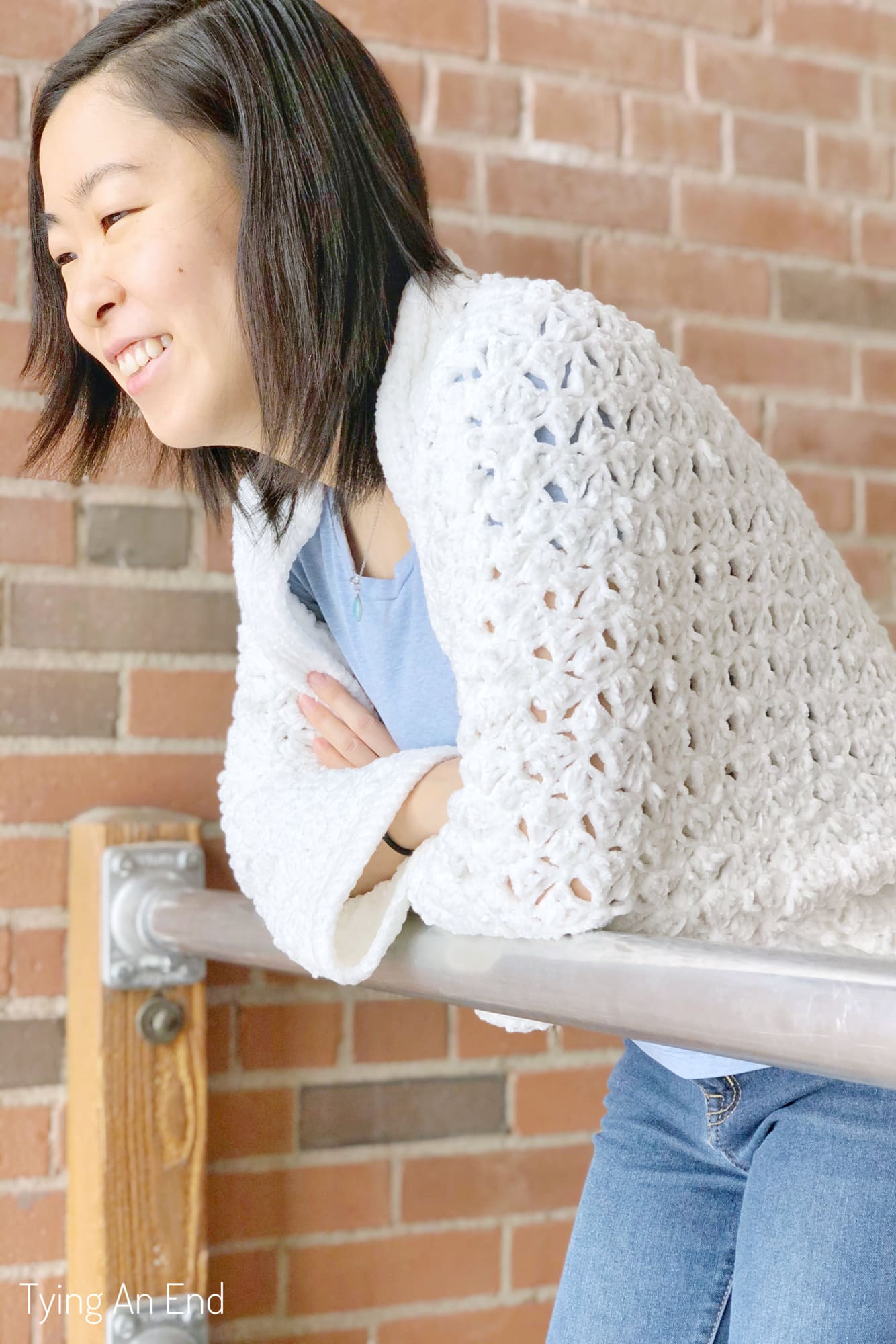 woman wearing white crochet c2c cocoon shrug in front of a brick wall